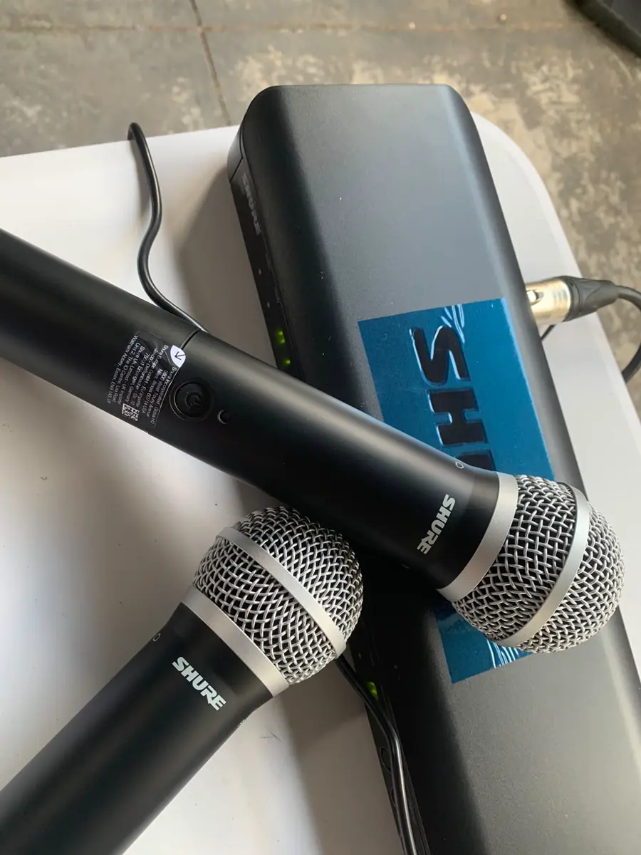 Two black Shure handheld microphones across a black audio receiver on a white surface