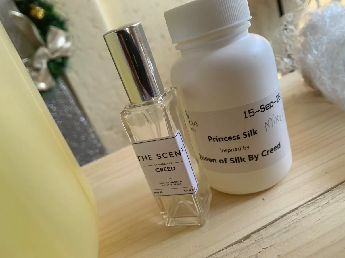 THE SCENT perfume bottle beside a Princess Silk bottle on a light wooden surface