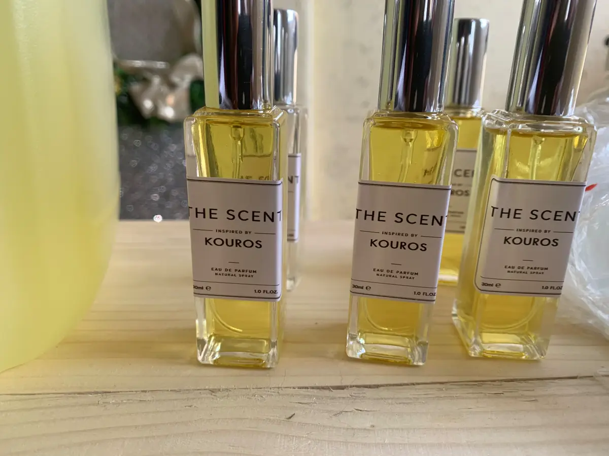Three THE SCENT perfume bottles inspired by Kouros Eau de Parfum on a light wooden surface