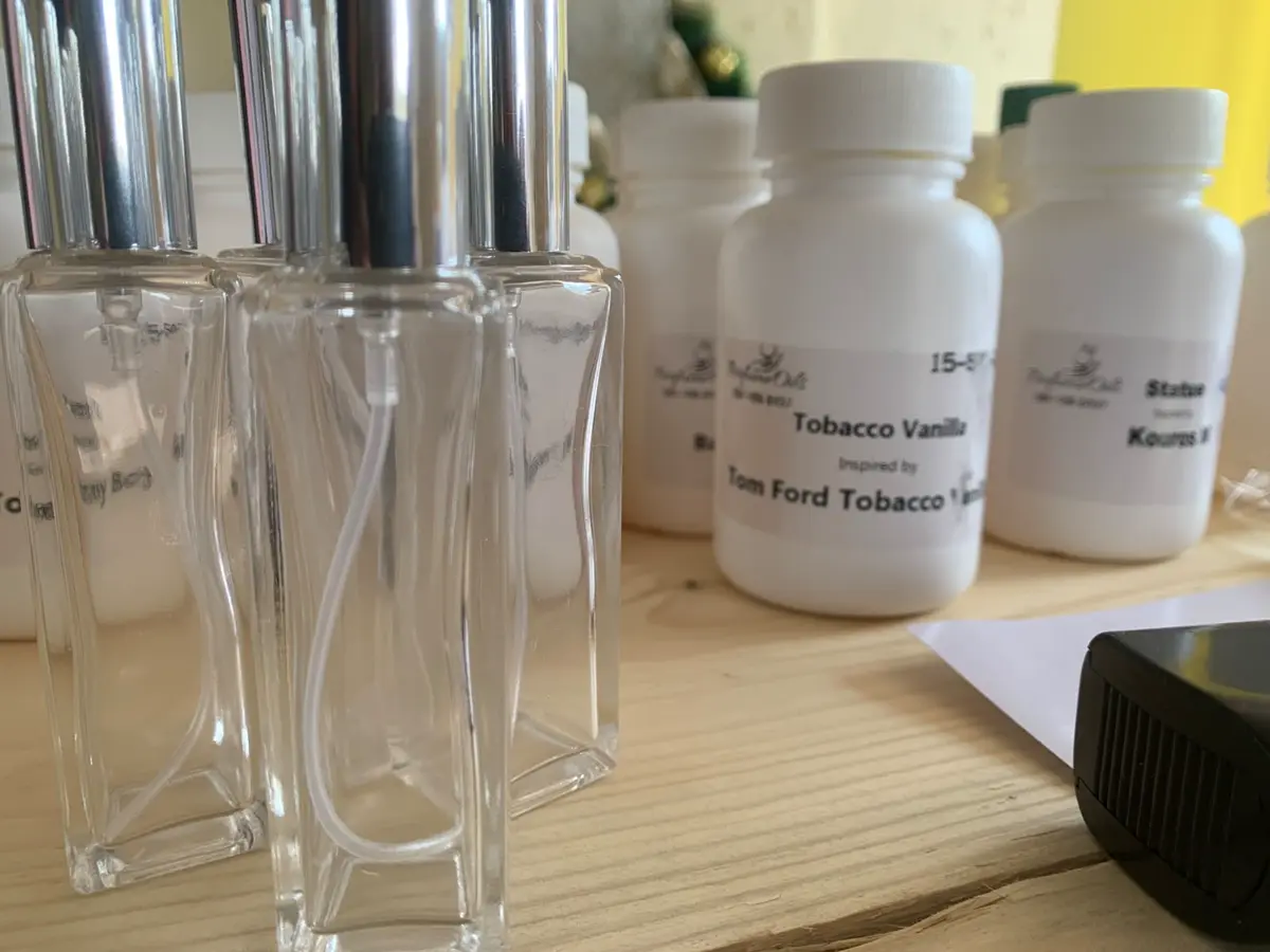 Clear glass pump bottles with Tom Ford Tobacco Vanilla and Kouros labels on a wooden tabletop